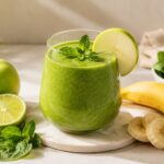 Zöld smoothie bébispenóttal, banánnal, zöld almával, mentával és lime-mal letisztult, napfényes konyhai környezetben.